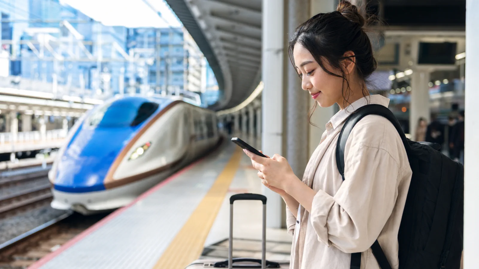 Traveler checking a phone beside a high-speed train in Japan