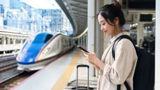 Traveler checking a phone beside a high-speed train in Japan